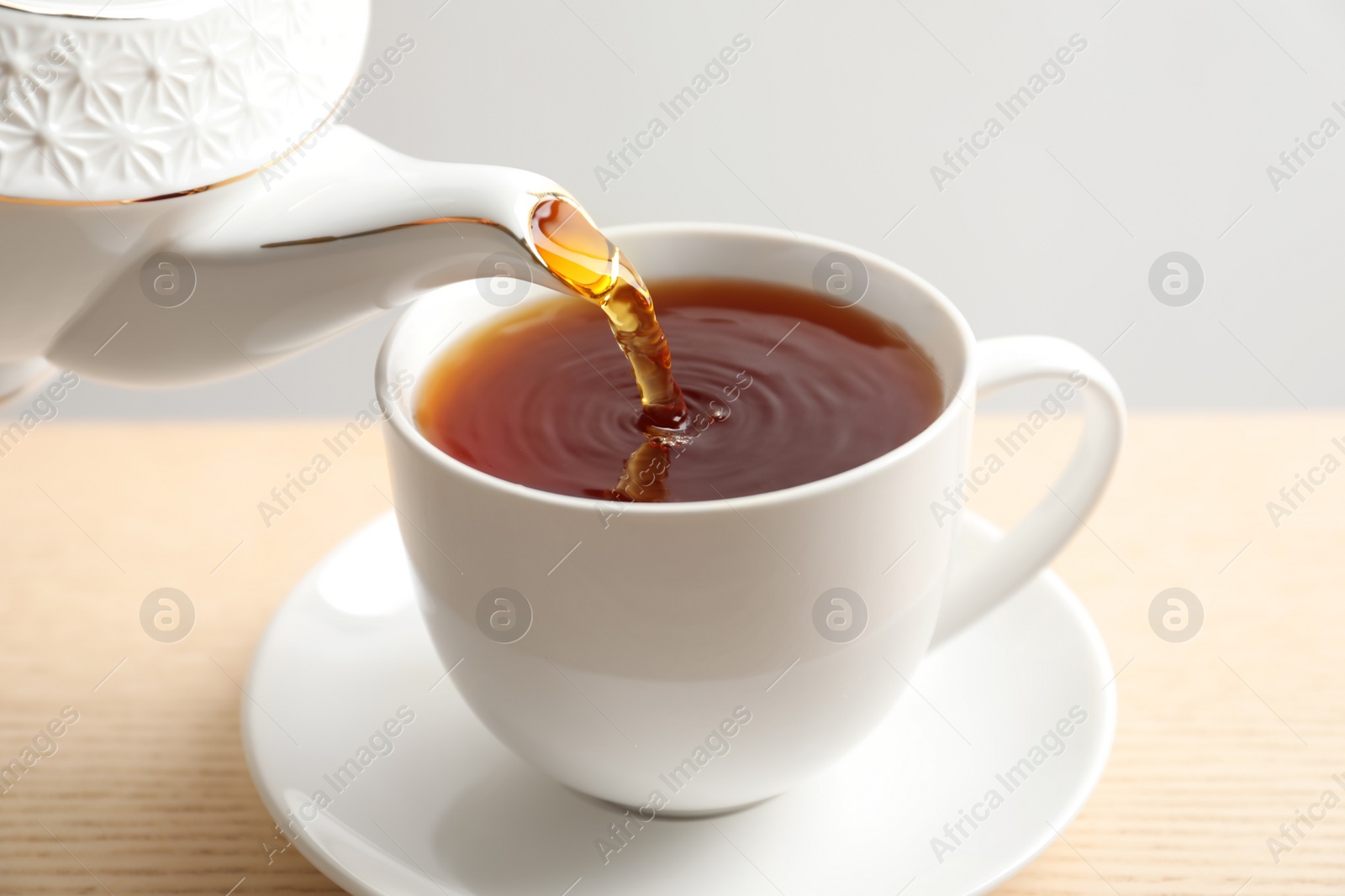 Photo of Pouring hot tea into porcelain cup on wooden table