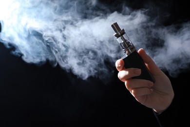 Photo of Woman holding electronic cigarette on black background, closeup. Space for text