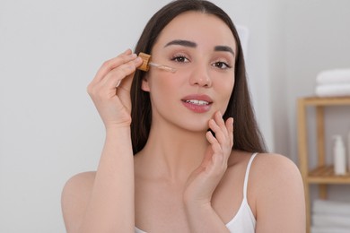 Photo of Woman applying essential oil onto face in bathroom