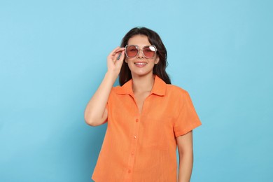 Photo of Happy beautiful woman with stylish sunglasses on light blue background