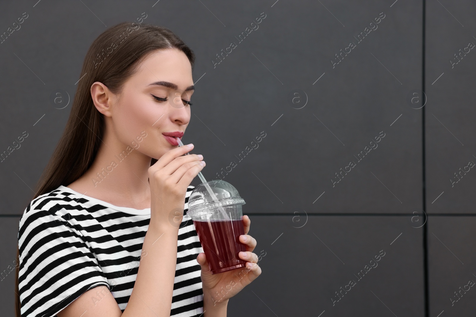 Photo of Young woman with plastic cup of fresh juice near brown wall, space for text