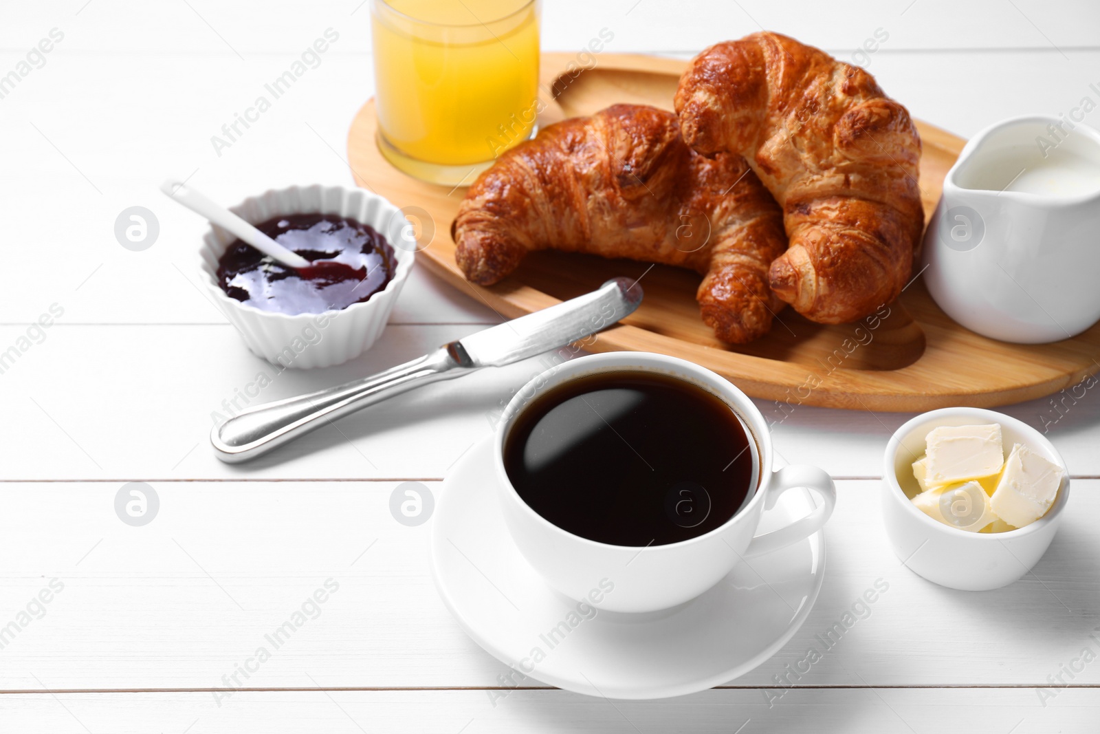 Photo of Fresh croissants, butter, jam and coffee on white wooden table. Tasty breakfast