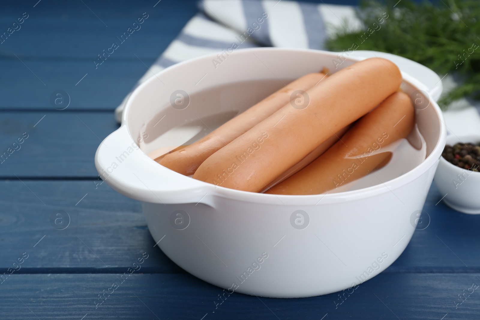 Photo of Bowl of delicious sausages, pepper and dill on blue wooden table, closeup