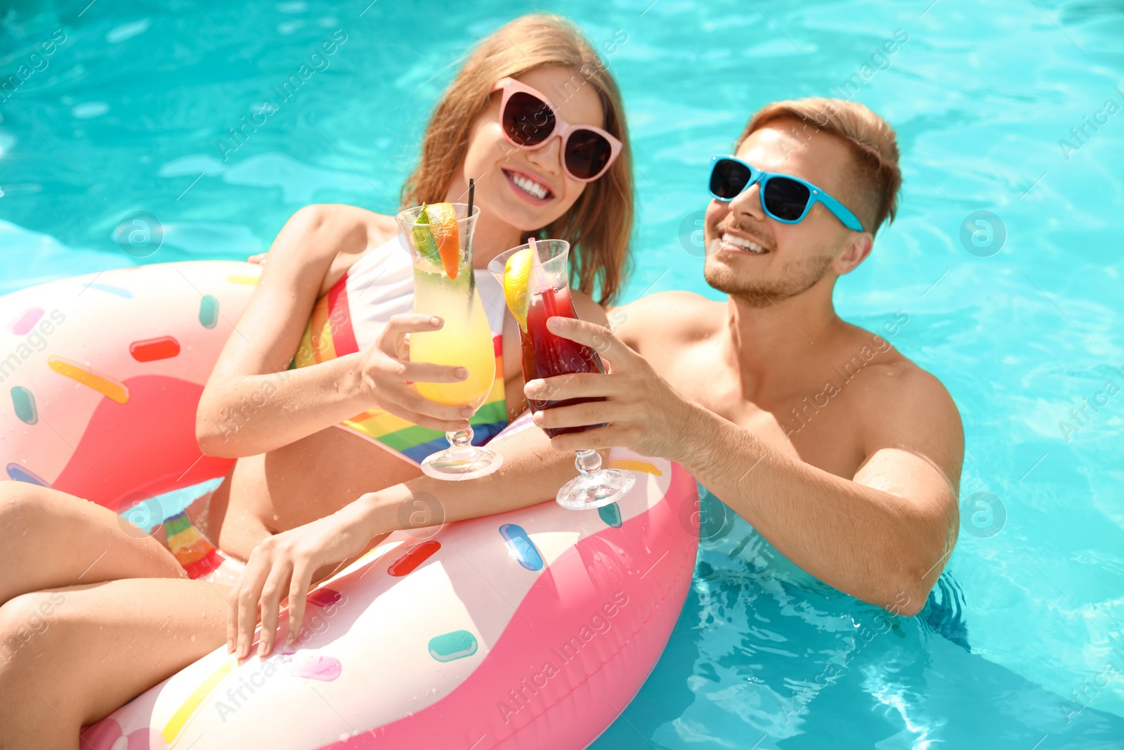 Photo of Young couple with cocktails in pool on sunny day