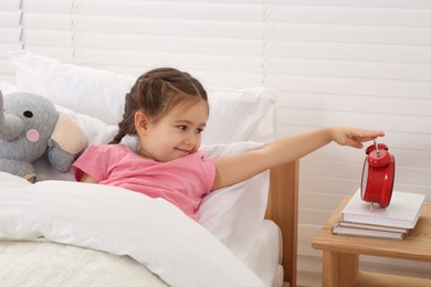 Photo of Cute little girl turning off alarm clock in cosy bedroom