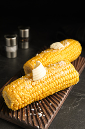 Photo of Delicious boiled corn with butter on wooden board