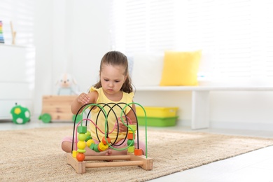 Photo of Cute little girl playing with bead maze on floor at home, space for text. Educational toy