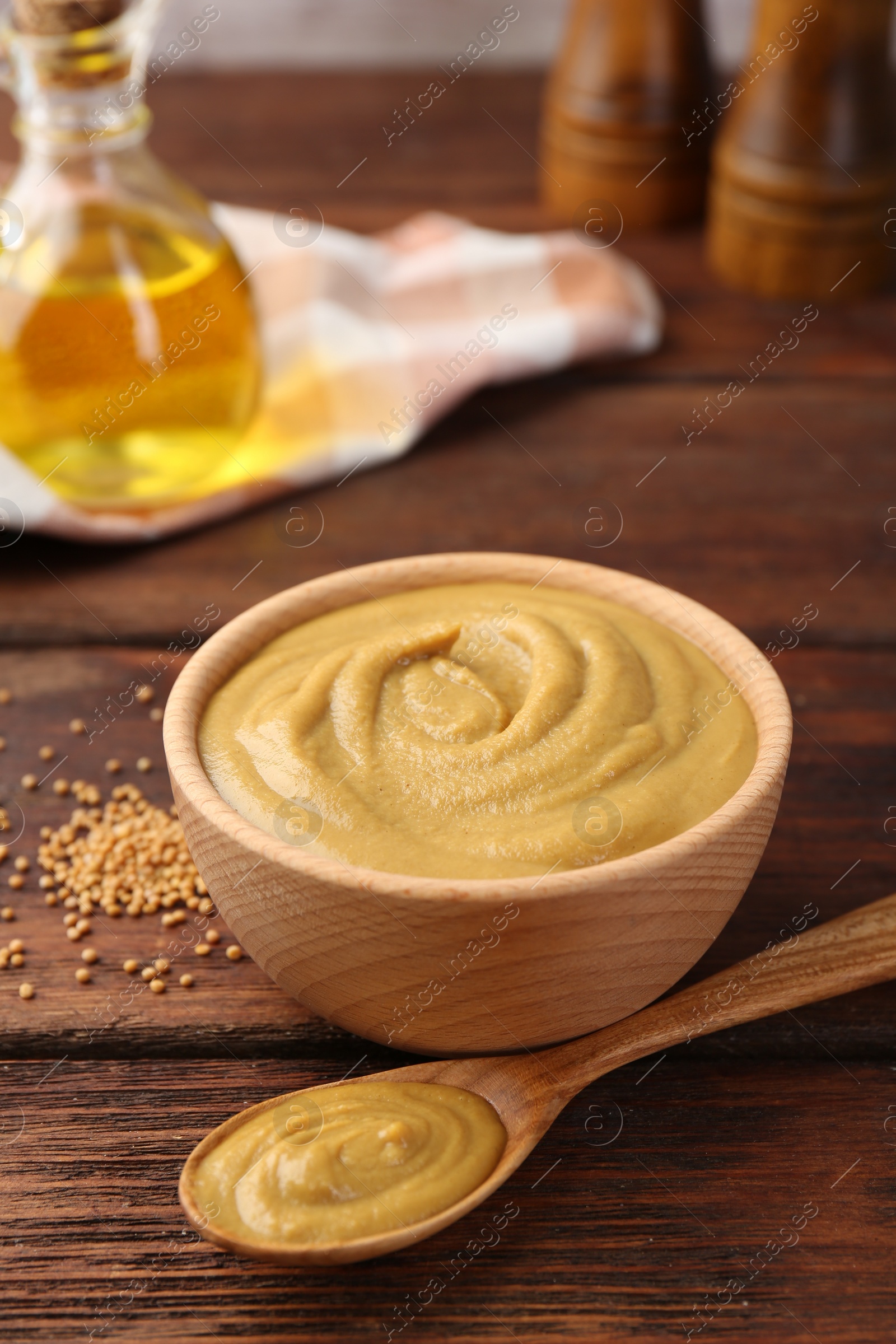 Photo of Bowl and spoon with tasty mustard sauce on wooden table, closeup