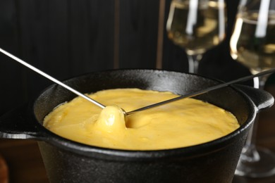 Photo of Dipping different products into fondue pot with melted cheese, closeup