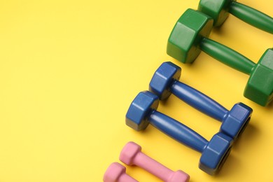 Photo of Different dumbbells on yellow background, above view. Space for text