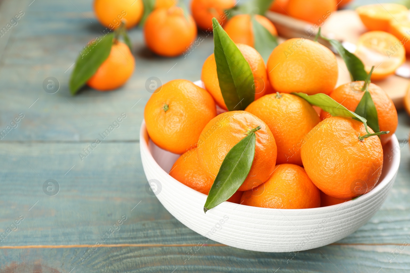 Photo of Fresh ripe tangerines with green leaves on blue wooden table, closeup