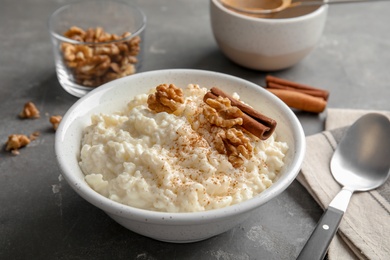 Creamy rice pudding with cinnamon and walnuts in bowl served on grey table