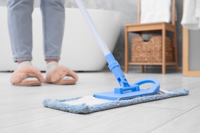 Photo of Woman cleaning parquet floor with mop in bathroom, closeup