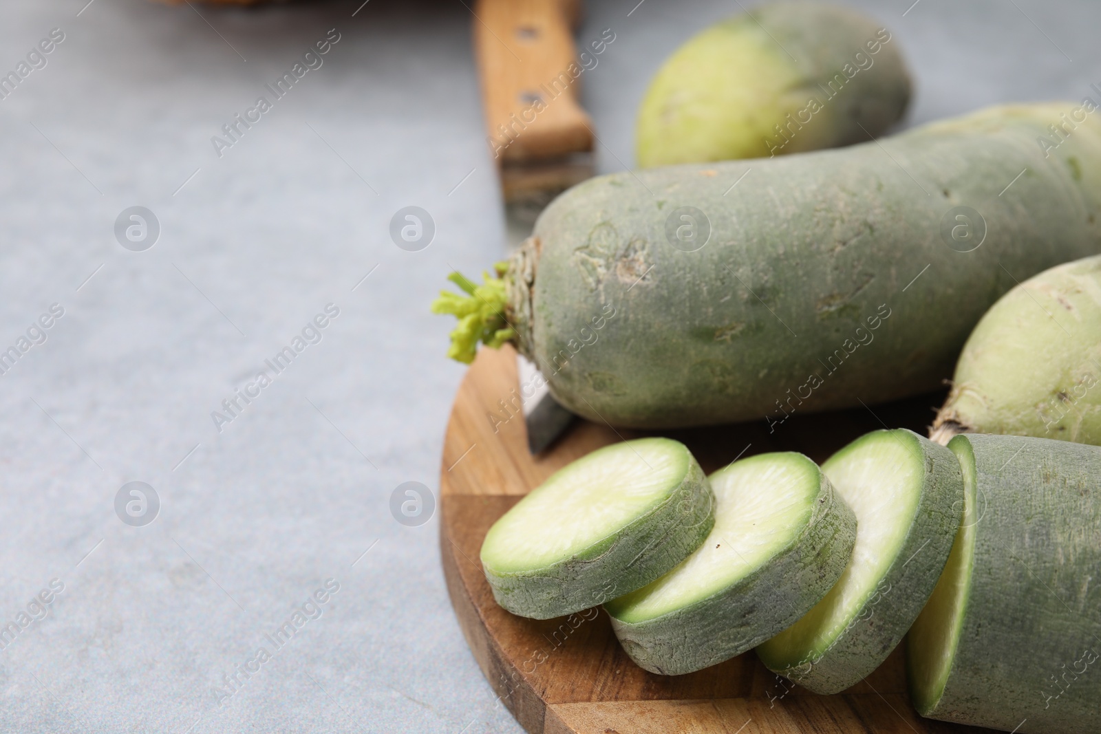 Photo of Green daikon radishes and knife on light grey table, closeup. Space for text