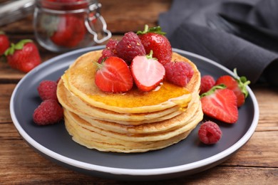 Tasty pancakes with fresh berries and honey on wooden table, closeup