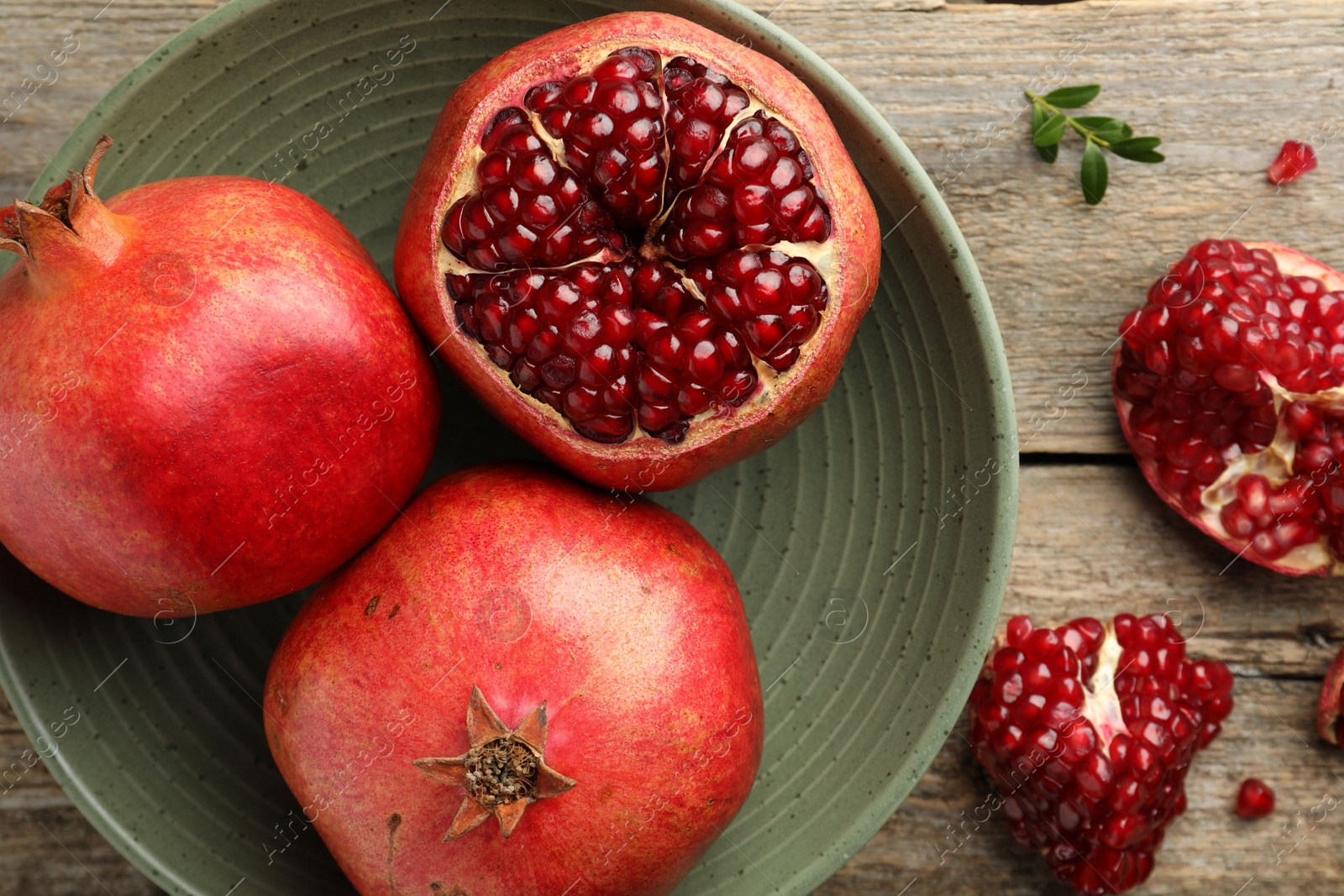 Photo of Fresh pomegranates and green leaves on wooden table, flat lay