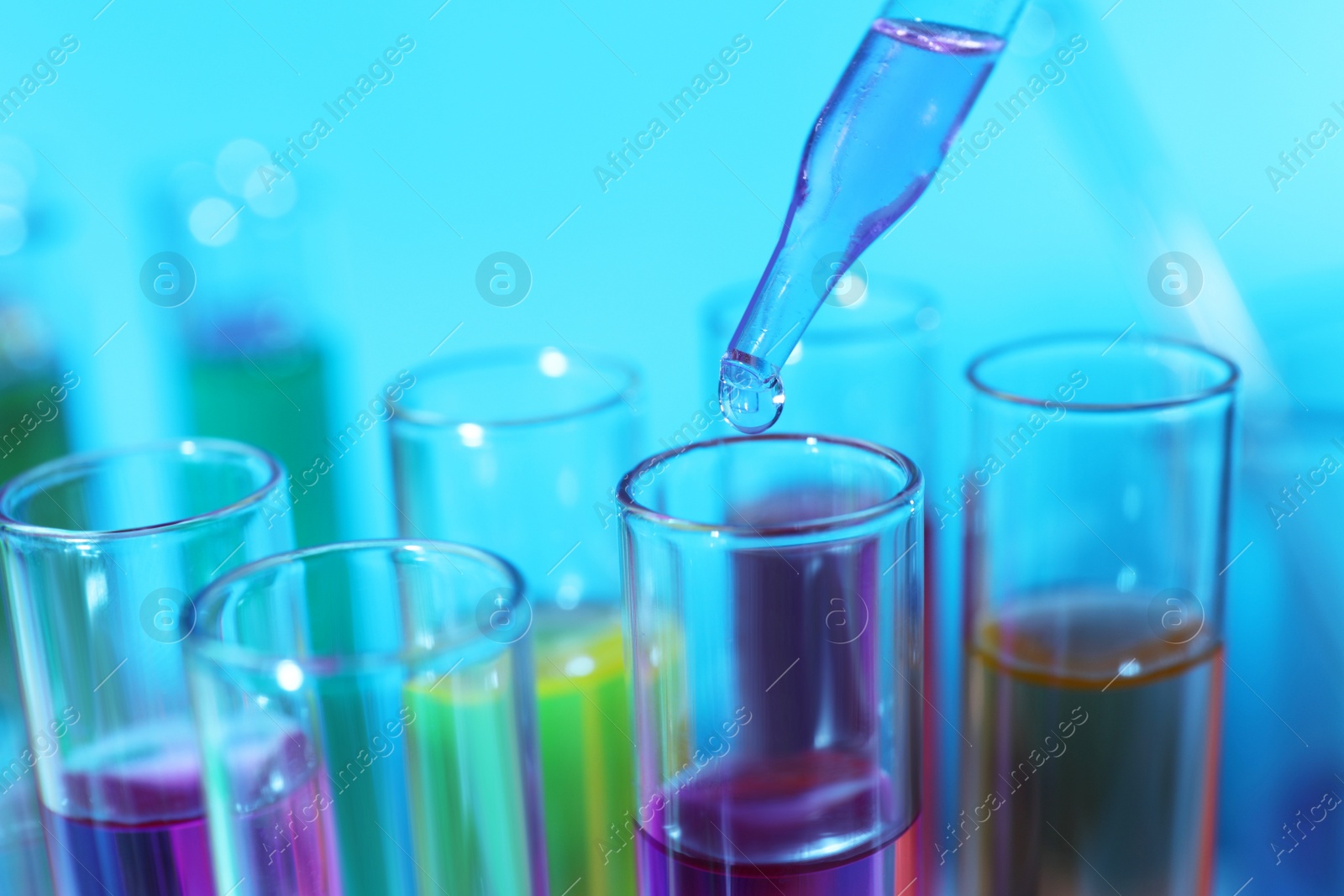 Photo of Dripping liquid from pipette into test tube on light blue background, closeup