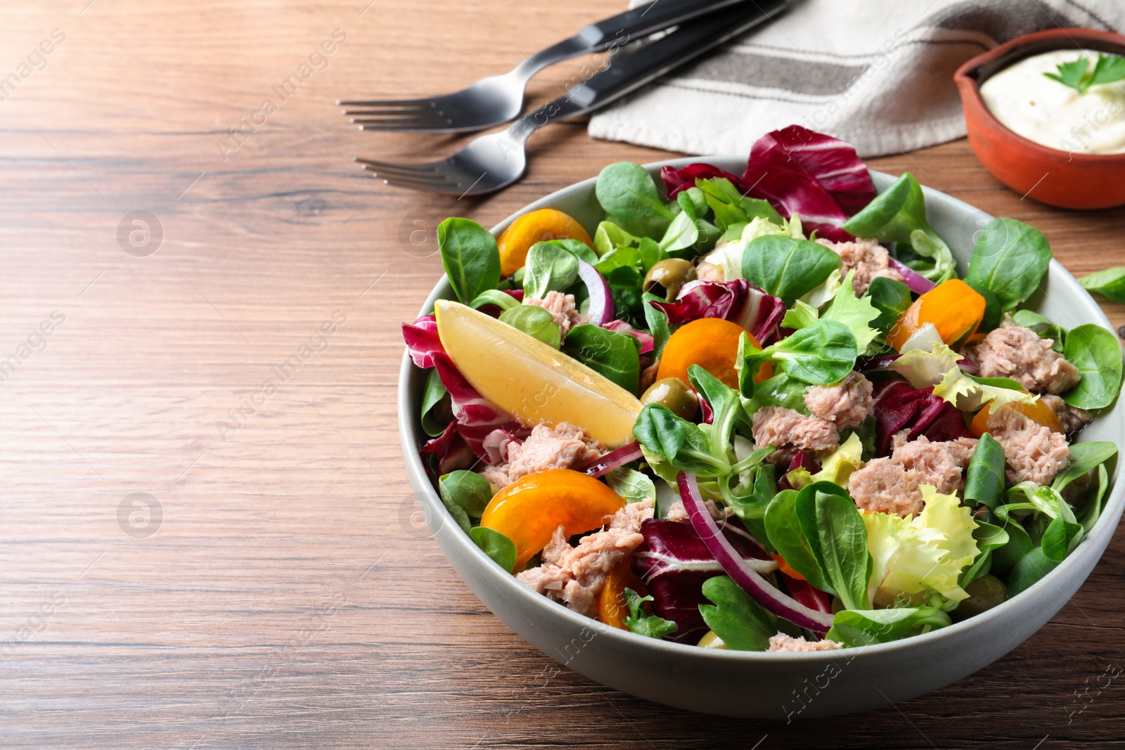 Photo of Bowl of delicious salad with canned tuna and vegetables on wooden table, space for text