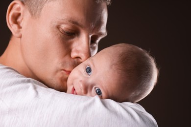 Photo of Happy father with his little baby on dark background, closeup