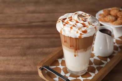 Glass of caramel macchiato on wooden table, space for text