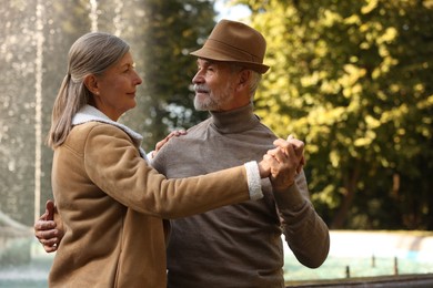 Affectionate senior couple dancing together near fountain outdoors. Romantic date