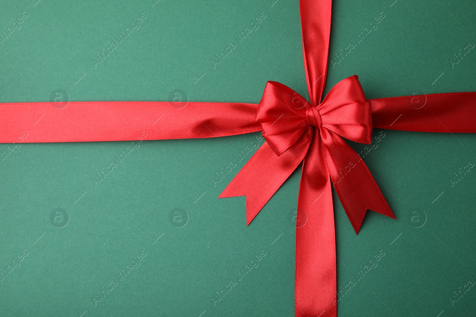 Photo of Red satin ribbon with bow on green background, top view