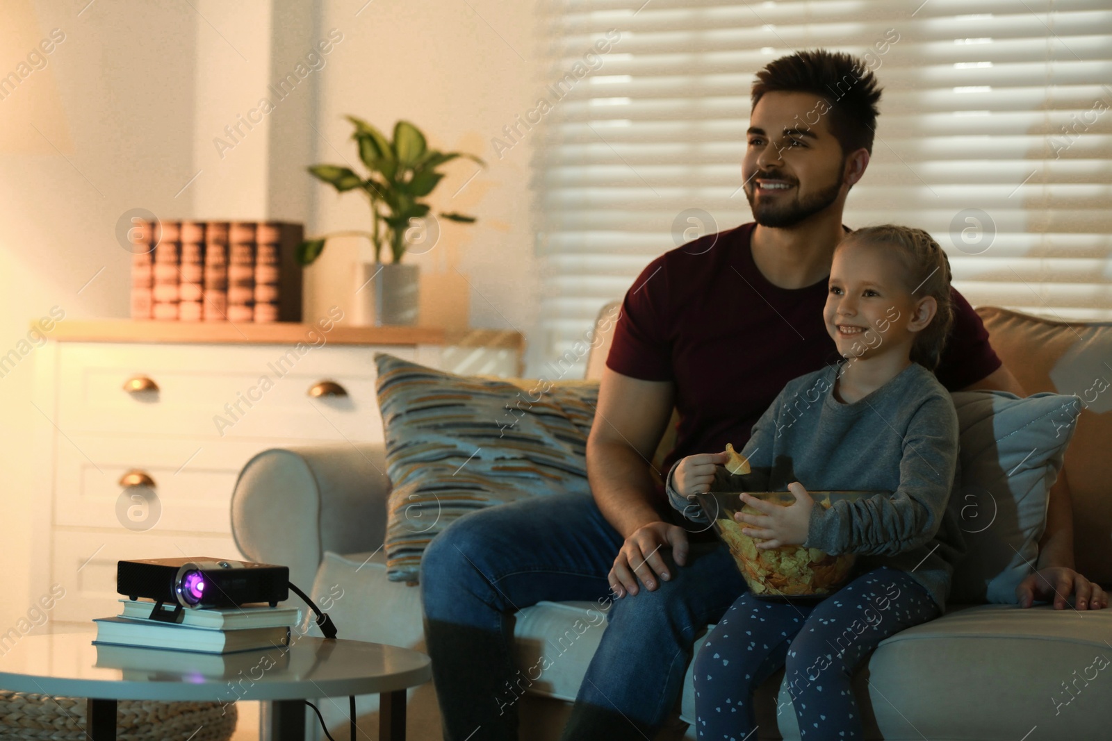 Photo of Young man and his daughter watching movie using video projector at home