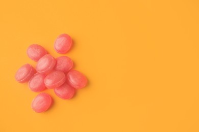 Many pink cough drops on orange background, flat lay. Space for text
