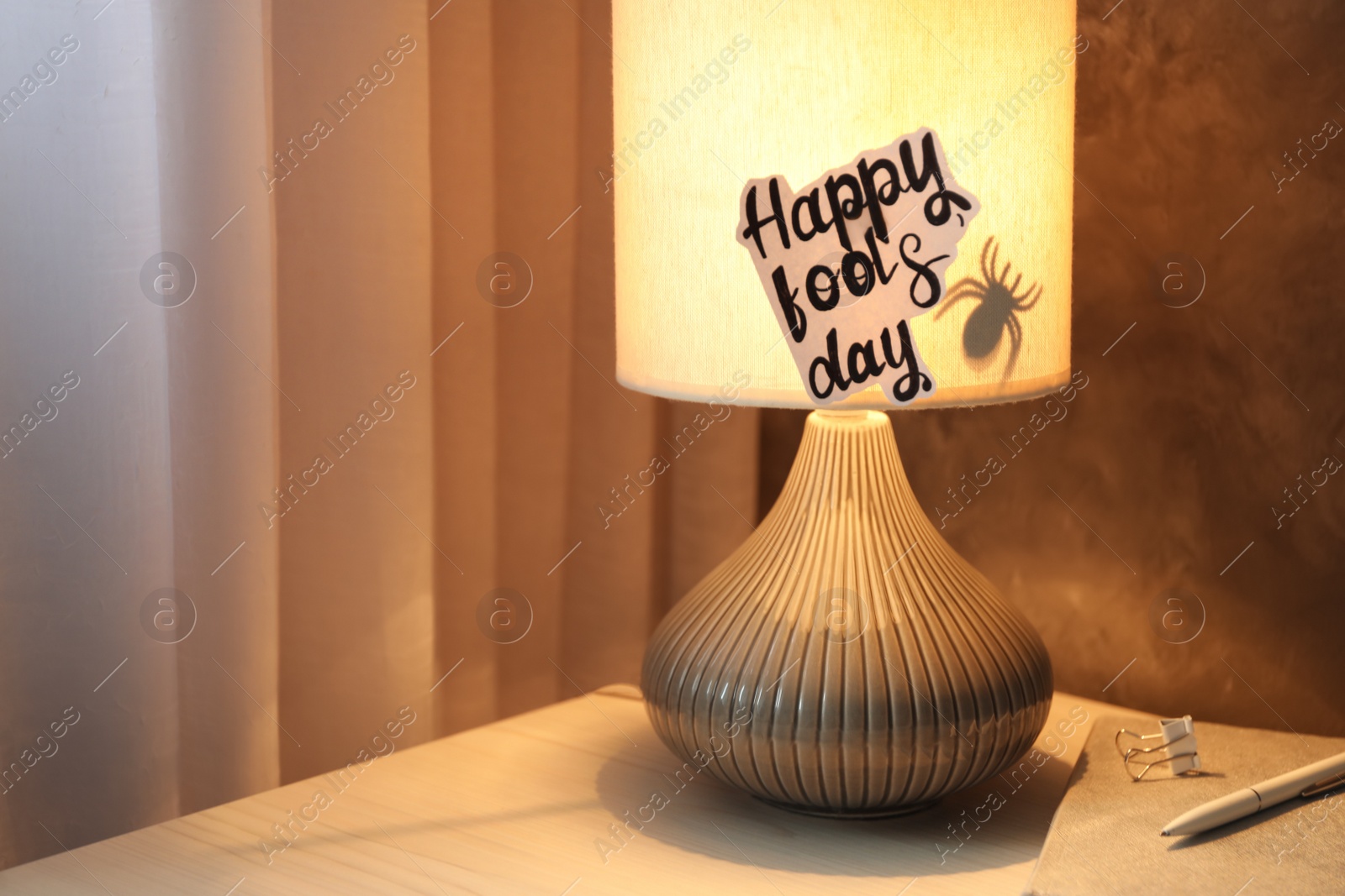 Photo of Glowing lamp with spider and words Happy Fool's Day on nightstand. Space for text