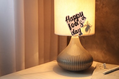 Photo of Glowing lamp with spider and words Happy Fool's Day on nightstand. Space for text