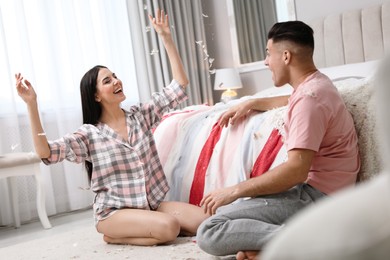 Photo of Happy couple having fun with flying feathers after pillow fight in bedroom