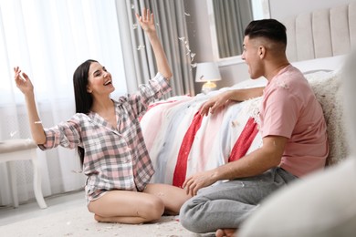 Happy couple having fun with flying feathers after pillow fight in bedroom