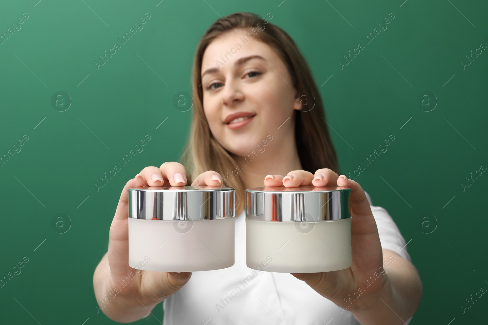 Photo of Cosmetologist with jars of cosmetic product on green background, selective focus