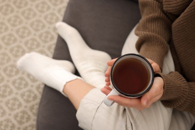 Photo of Woman in warm socks relaxing with cup of tea at home, above view