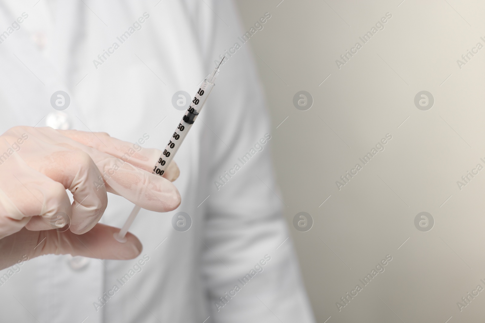 Photo of Doctor holding syringe on grey background, closeup. Space for text