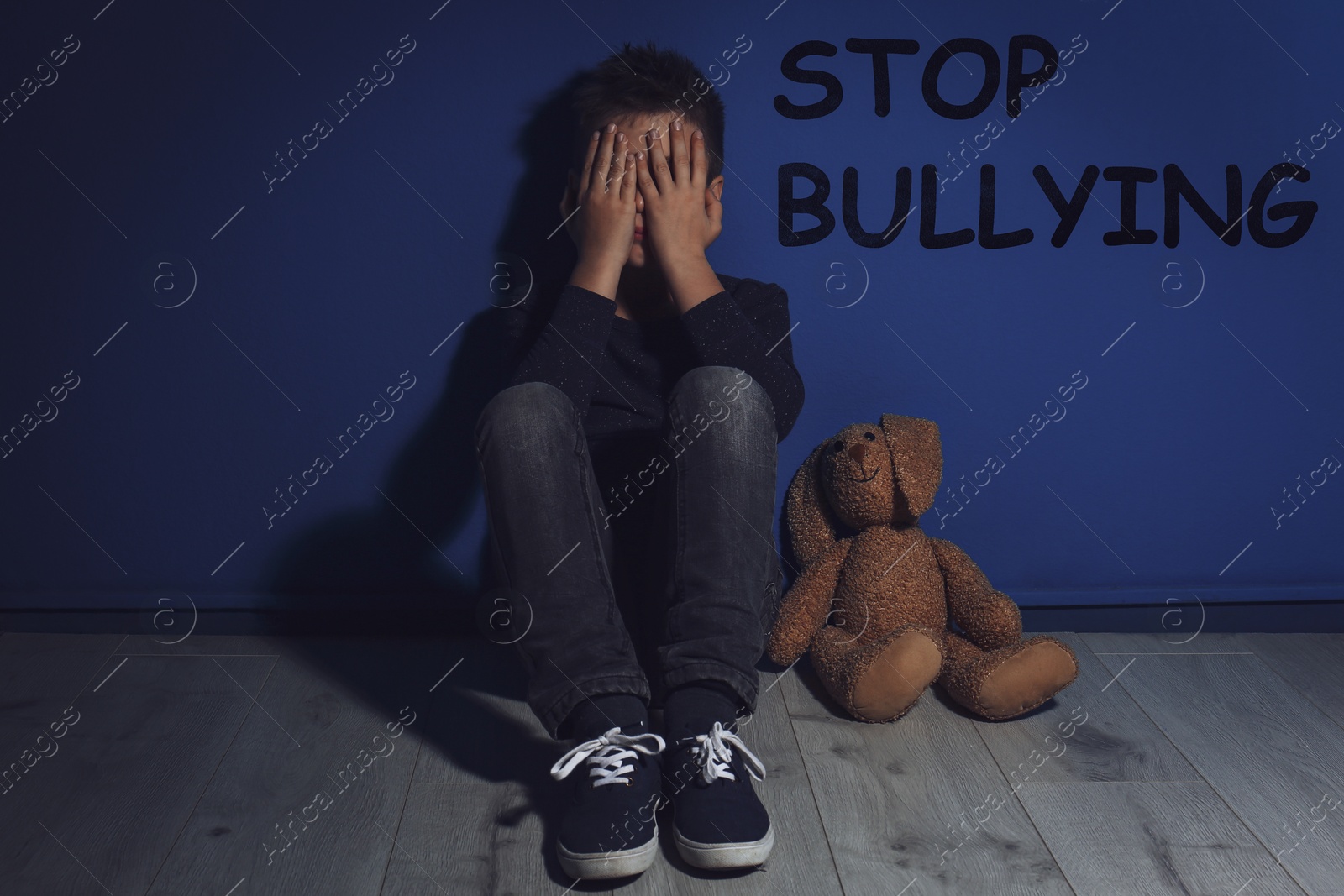 Image of Message STOP BULLYING and abused little boy crying near blue wall