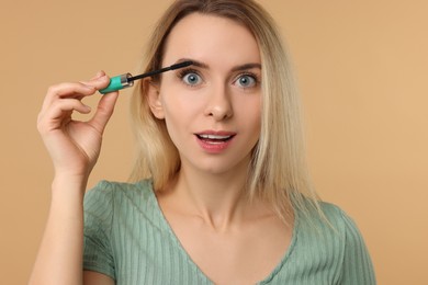 Photo of Beautiful woman applying mascara on beige background