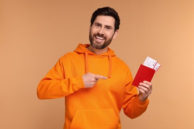 Smiling man pointing at passport and tickets on beige background