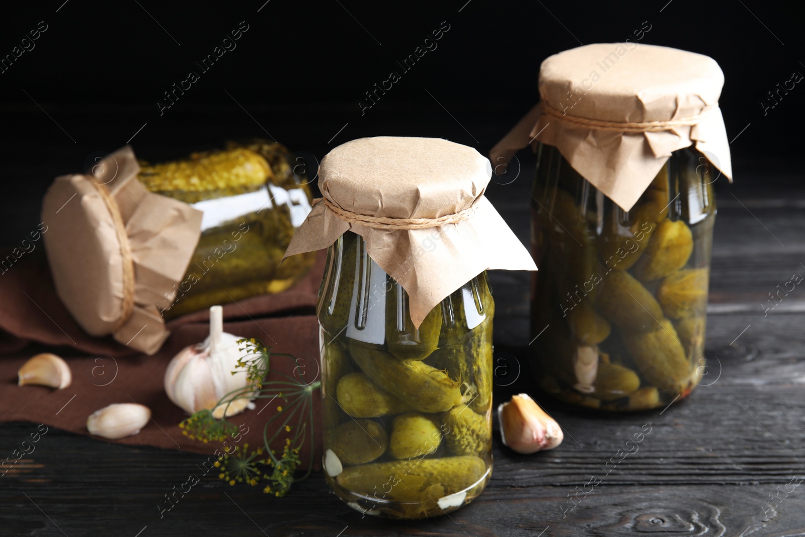 Photo of Jars with pickled cucumbers on black wooden table