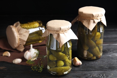 Jars with pickled cucumbers on black wooden table