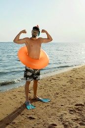 Man with flippers, inflatable ring and goggles on sea beach
