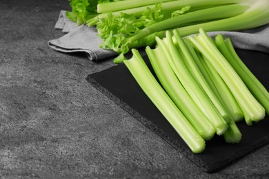 Photo of Board with fresh green cut celery on grey table, space for text