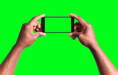 Image of African American man holding smartphone with green screen on color background, closeup. Mockup for design