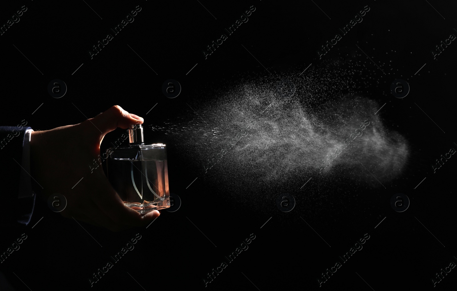 Photo of Man spraying luxury perfume on black background, closeup