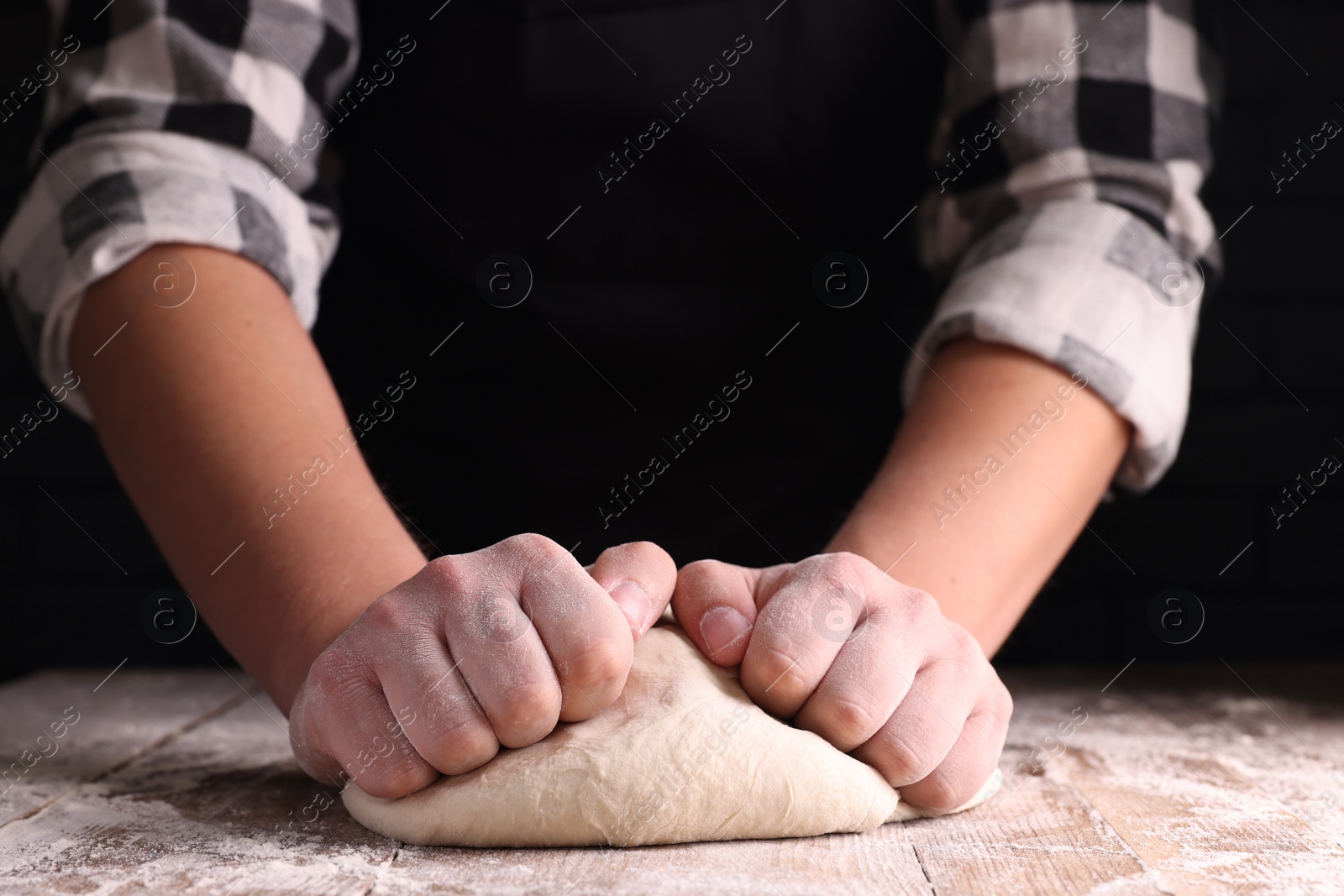 Photo of Man kneading dough at wooden table on dark background, closeup