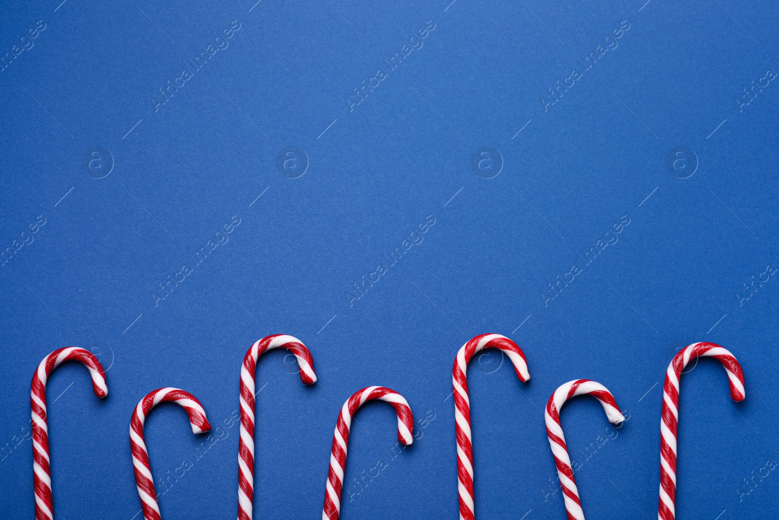 Photo of Many sweet Christmas candy canes on blue background, flat lay. Space for text