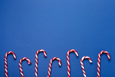 Photo of Many sweet Christmas candy canes on blue background, flat lay. Space for text