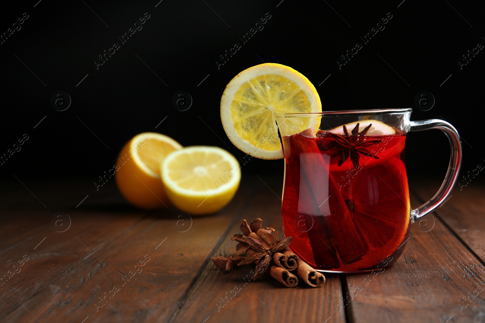 Photo of Cup with red mulled wine on wooden table against dark background