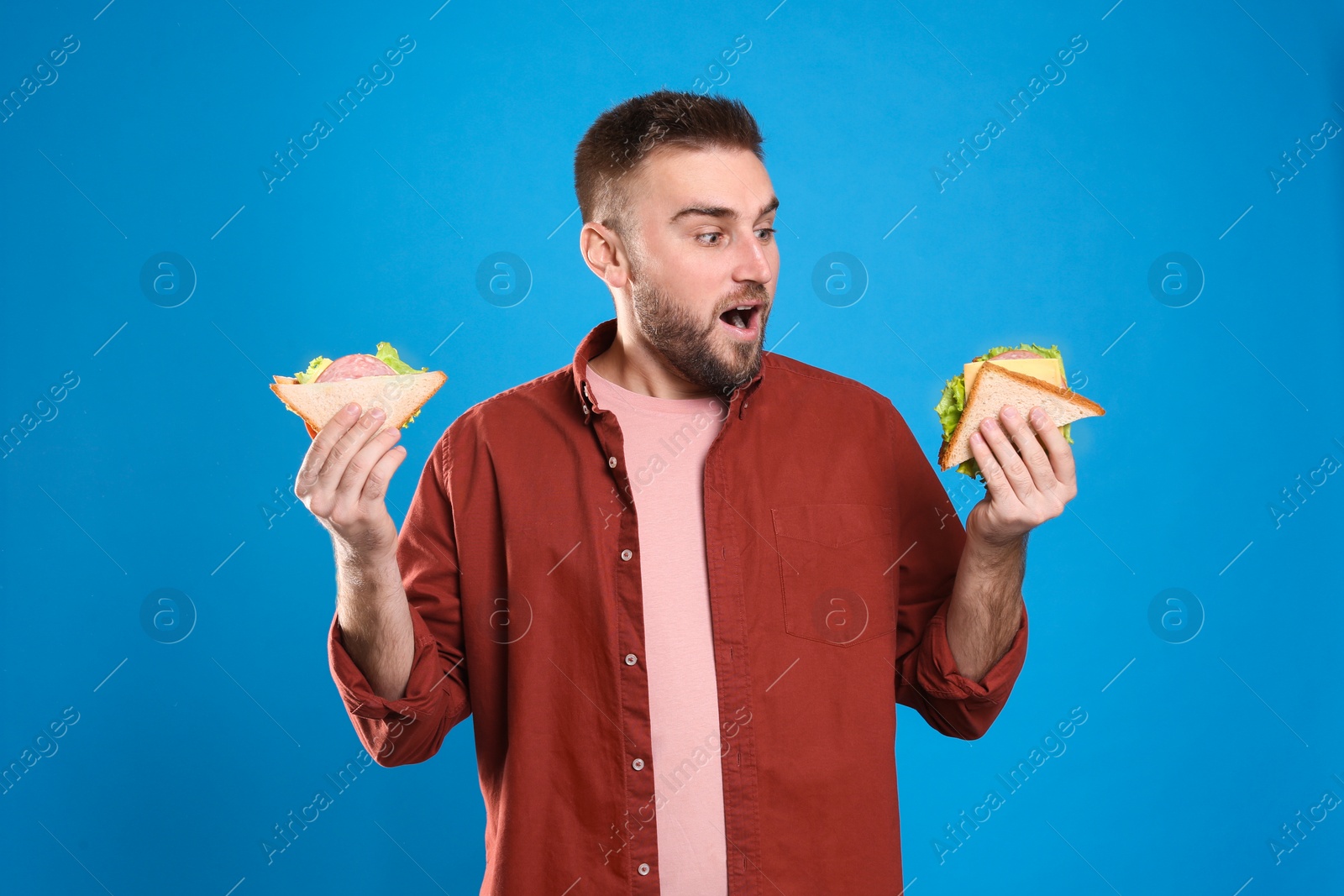 Photo of Young man with tasty sandwiches on light blue background