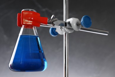 Photo of Retort stand and laboratory flask with liquid on grey background, closeup